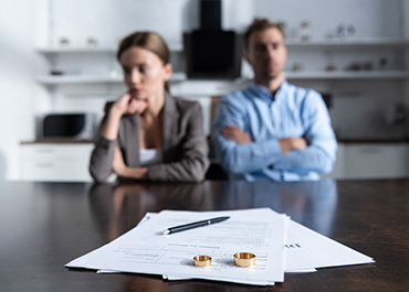 Couple sitting apart with wedding rings and legal papers, representing contested divorce.