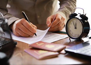 Person signing immigration forms next to a clock, illustrating the asylum filing deadline.