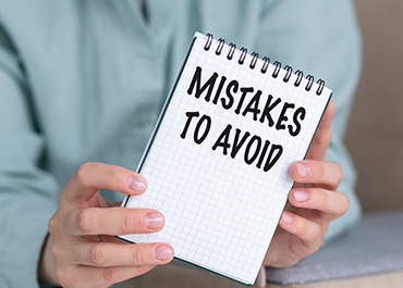 Hand holding a notepad titled 'Mistakes To Avoid' for legal consultation guidance.